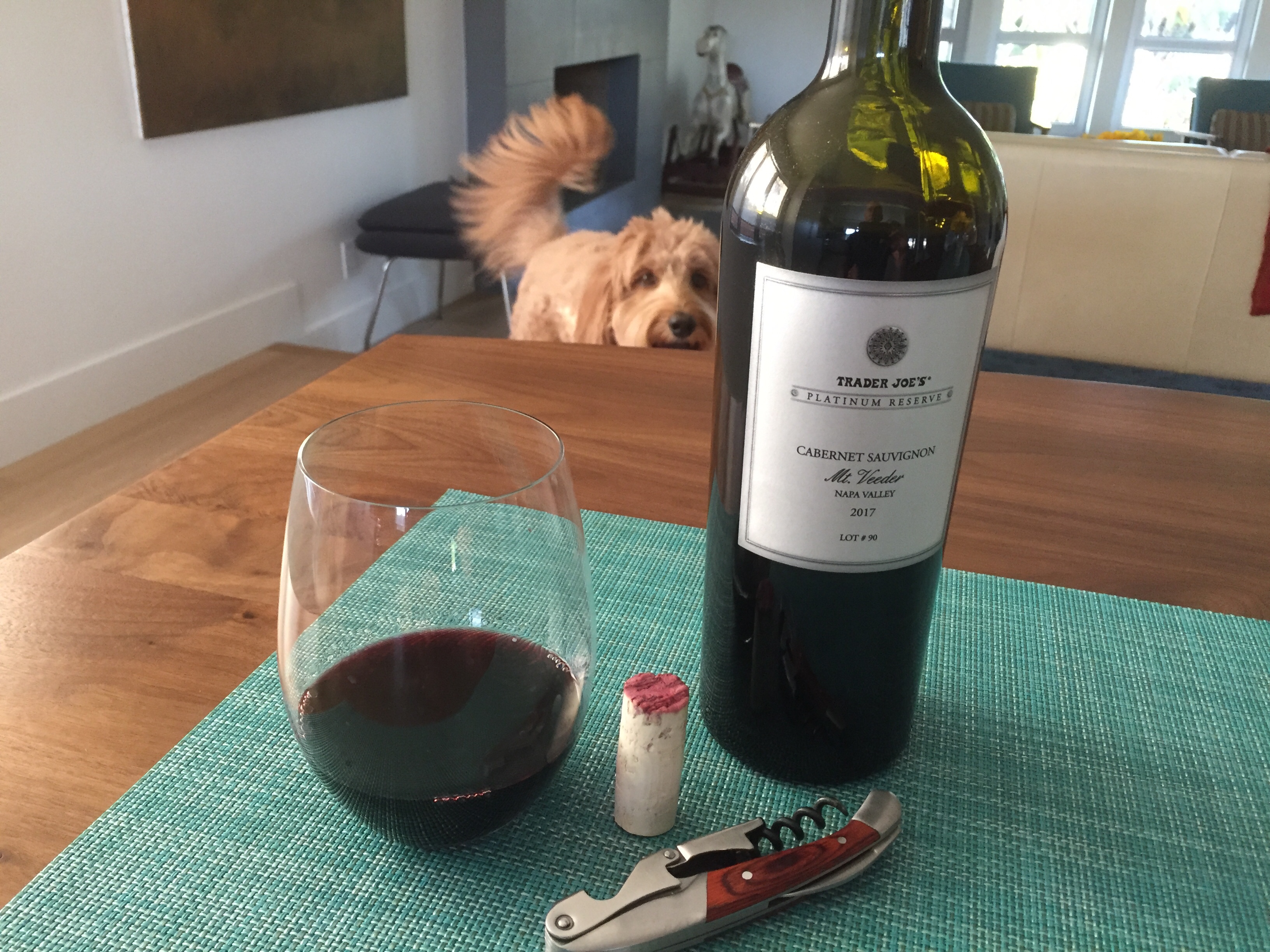 Glass and bottle of Trader Joe's 2017 Platinum Reserve Mt. Veeder Napa Valley Cabernet Sauvignon with a Labradoodle photobomer