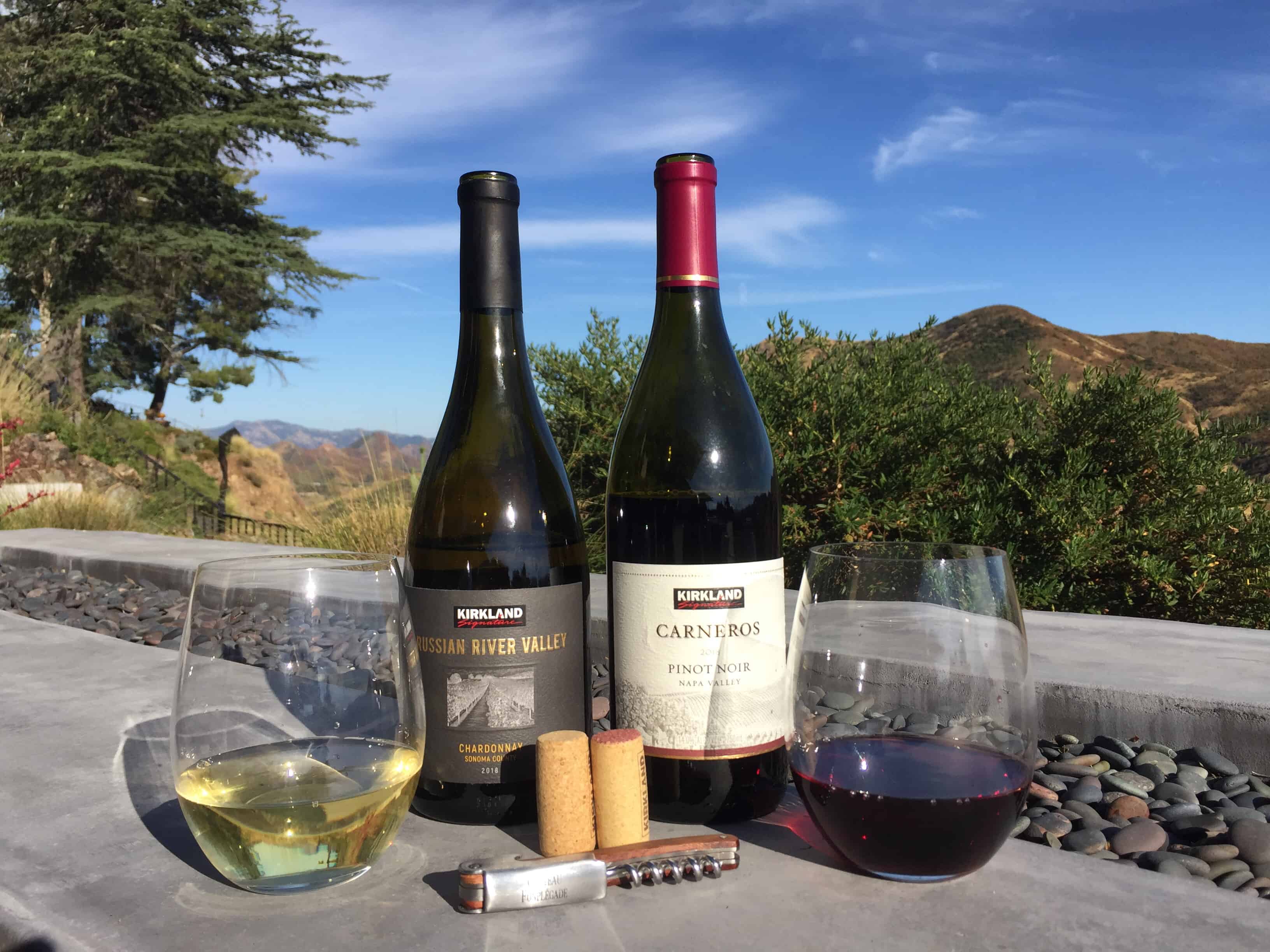 Bottles and glasses of Kirkland Signature Chardonnay and Pinot Noir