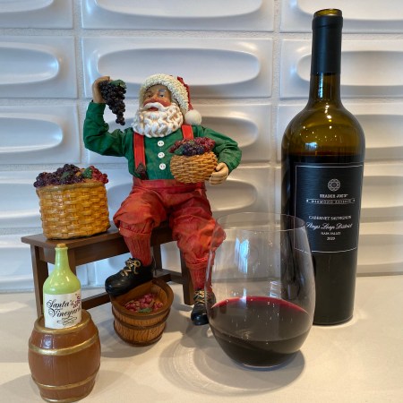 A Santa statuette alongside a glass and bottle ofthe 2020 Trader Joe's Diamond Reserve Cabernet Sauvignon from the esteemed Stag's Leap district of Napa Valley.