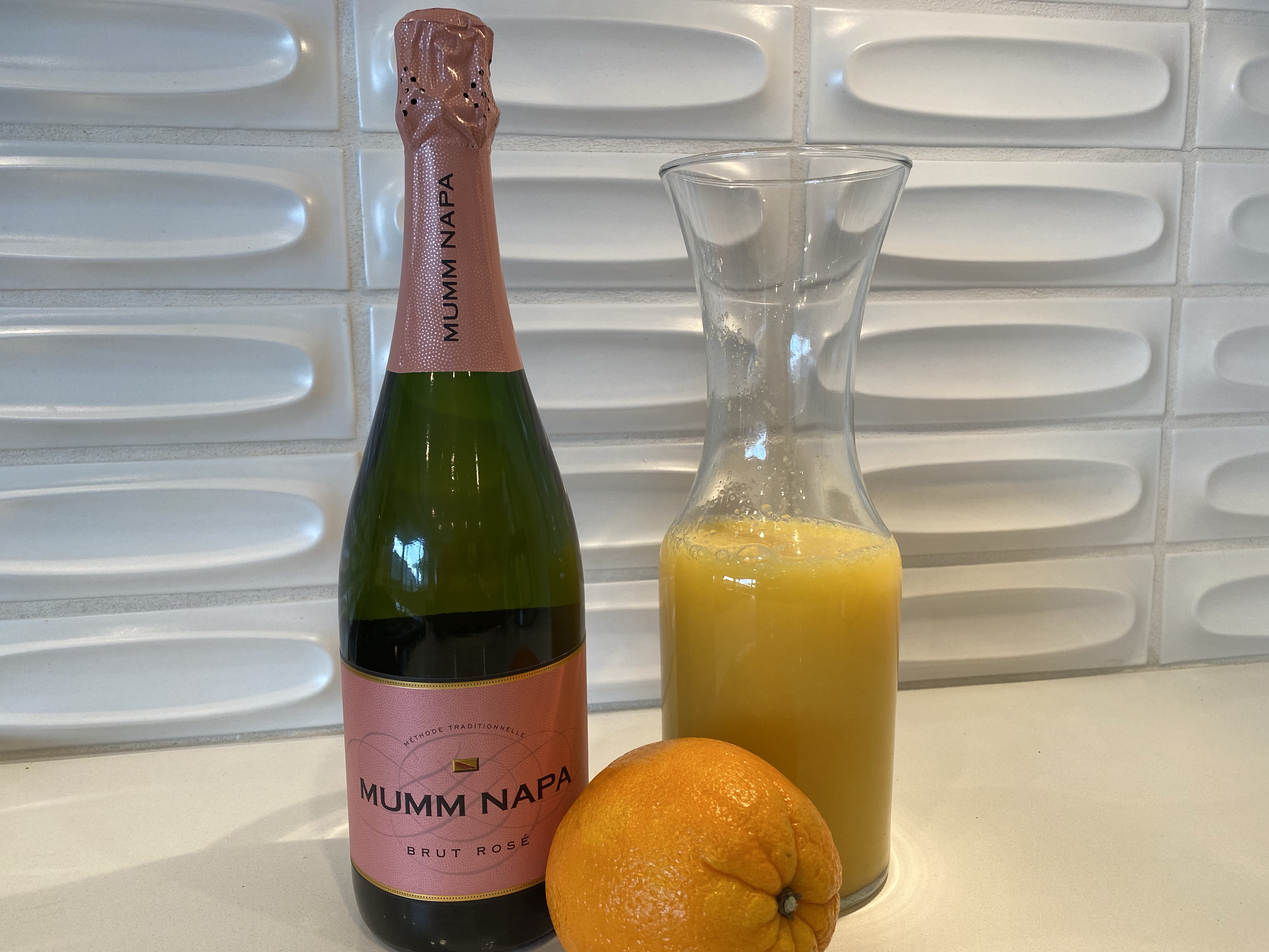 A holiday morning Mimosa kit, Mumm sparkling wine, a carafe of OJ and orange for a garnish.